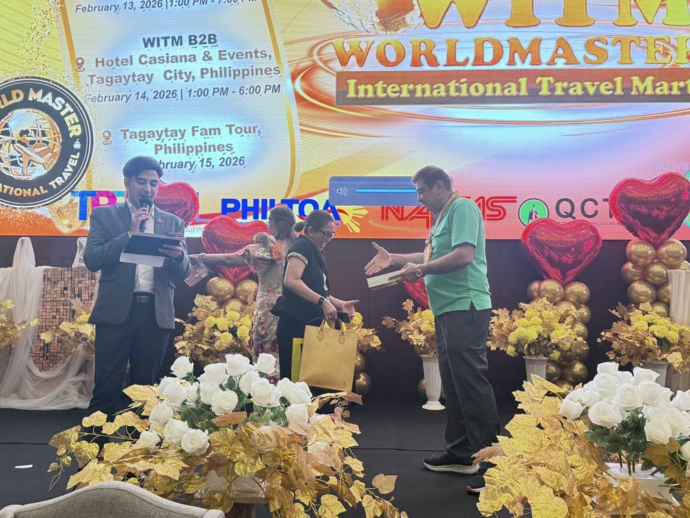 A delegate receiving a plaque on stage from an official wearing a medal lei, heart-shaped balloons and gold florals dressing the stage.